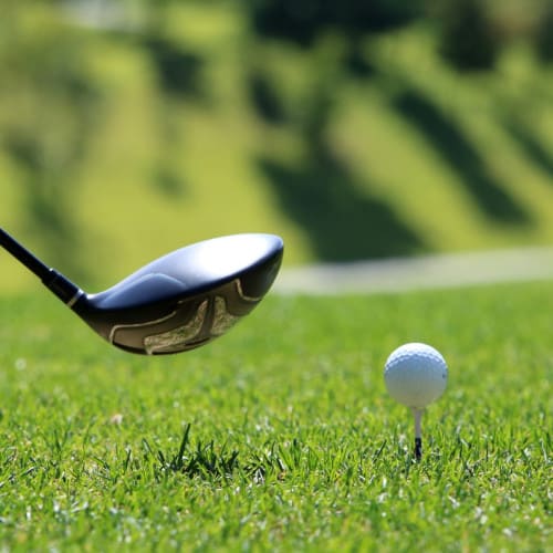 Close up of a golf club about to strike a golf ball off the tee.